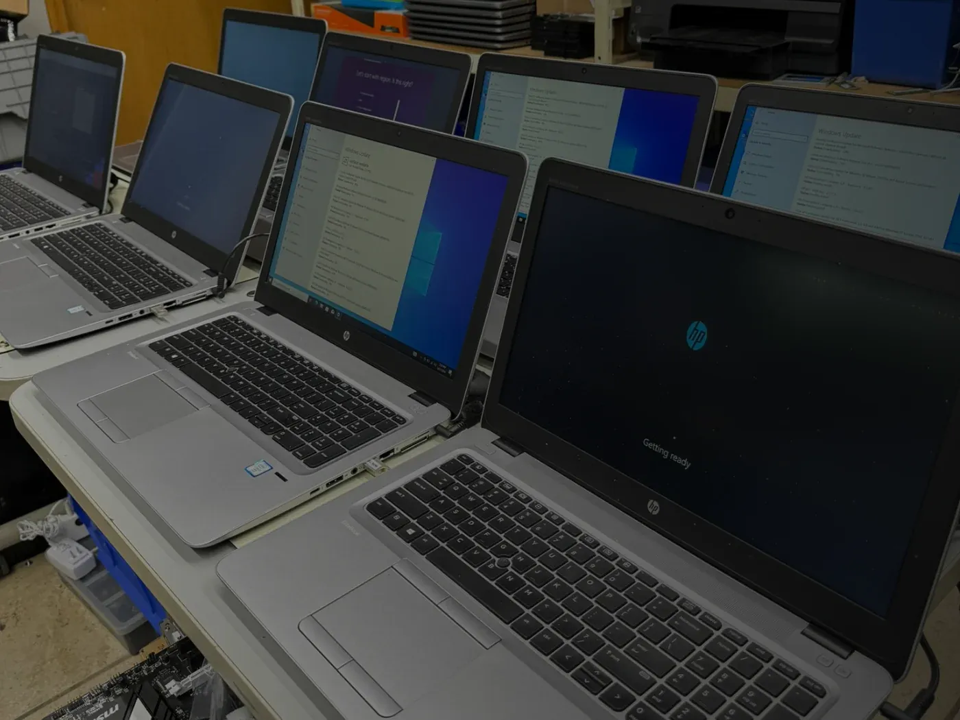 A row of refurbished HP laptops on a workbench, mid-setup, running Windows Update and first-boot screens
